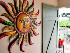 Large sun decoration hangs on a wall next to an open door leading into greenhouse
